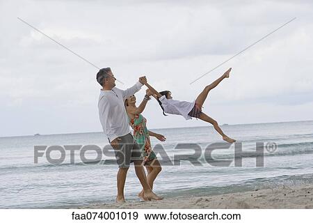 Stock Photo - Parents swinging daughter while walking on beach. Fotosearch