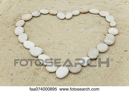 Stock Photography - Pebbles arranged in heart shape on sand. Fotosearch