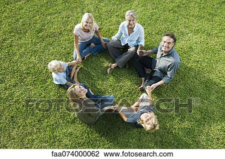 People sitting in circle on grass holding hands looking up at camera View Large Photo Image Stock Image - People sitting in circle on grass holding hands looking up at camera. Fotosearch