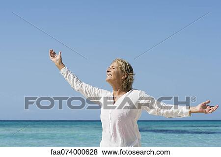Senior woman by sea with arms outstretched, portrait View Large Photo Image Stock Photo - Senior woman by sea with arms outstretched, portrait. Fotosearch