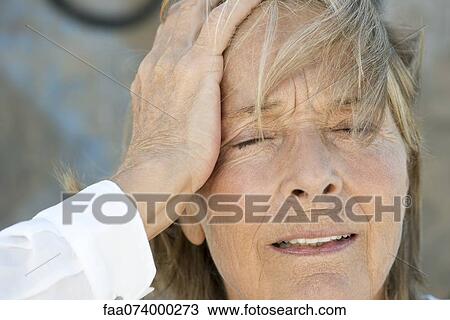 Stock Image - Senior woman holding head, eyes closed. Fotosearch