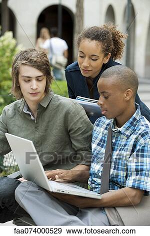Stock Photo - University students discussing homework on campus with laptop computer. Fotosearch