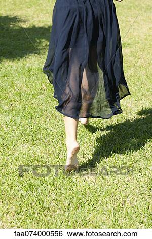 Stock Photograph - Woman barefoot in grass, rear view. Fotosearch