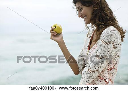 Stock Photo - Woman eating apple at the beach. Fotosearch