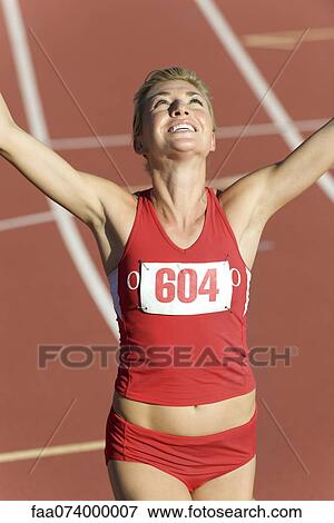 Stock Photo - Woman running on track with arms raised in victory. Fotosearch