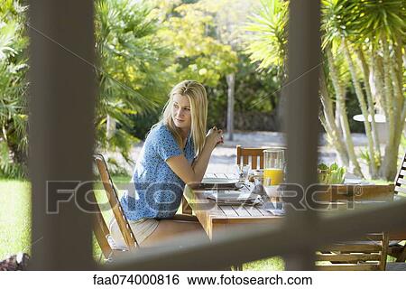 Stock Photograph - Woman sitting at outdoor table, gazing over shoulder. Fotosearch