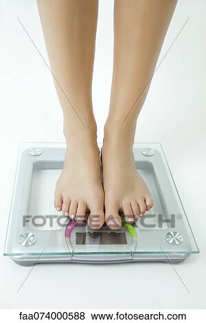 Stock Photo - Woman weighing herself on bathroom scale, low section. Fotosearch