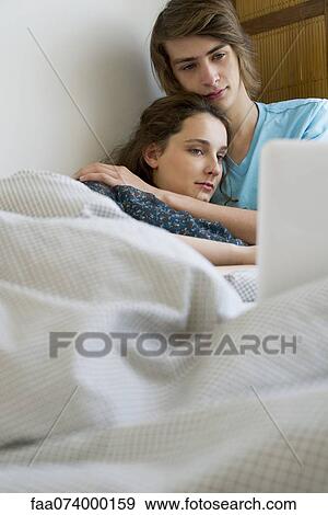 Stock Photo - Young couple relaxing together in bed with laptop computer. Fotosearch