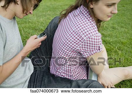 Young couple sitting together on grass, man text messaging View Large Photo Image Stock Image - Young couple sitting together on grass, man text messaging. Fotosearch