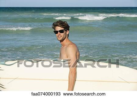 Young man carrying surfboard View Large Photo Image Stock Image - Young man carrying surfboard. Fotosearch
