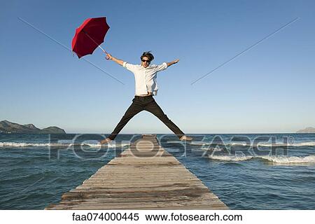 Young man jumping on pier with umbrella View Large Photo Image Stock Photography - Young man jumping on pier with umbrella. Fotosearch