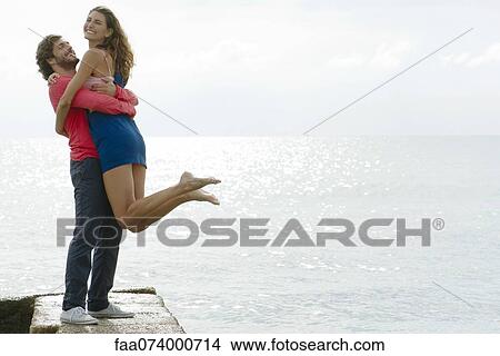 Young man lifting girlfriend up by water, portrait View Large Photo Image Picture - Young man lifting girlfriend up by water, portrait. Fotosearch