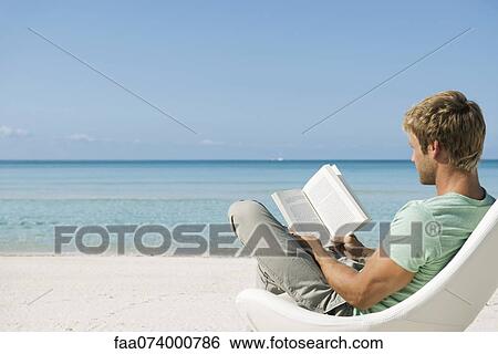 Stock Photograph - Young man reading book on beach. Fotosearch