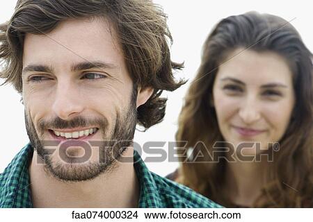 Picture - Young man smiling, young woman in background. Fotosearch