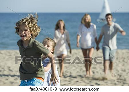 Young siblings playing at the beach, family in background View Large Photo Image Stock Photo - Young siblings playing at the beach, family in background. Fotosearch