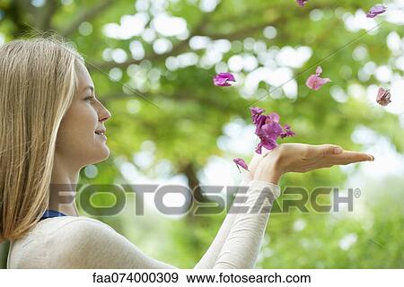 Stock Photo - Young woman catching falling petals, side view. Fotosearch