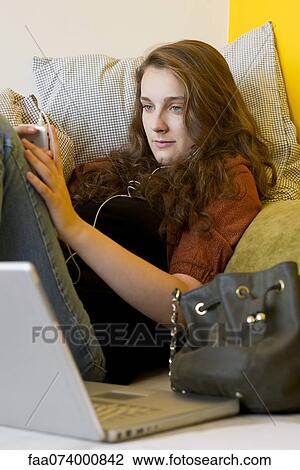 Stock Image - Young woman listening to MP3 player. Fotosearch