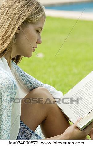 Stock Image - Young woman reading book outdoors. Fotosearch