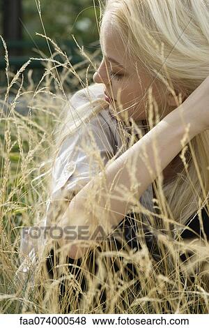 Stock Photo - Young woman sitting in tall grass with eyes closed. Fotosearch