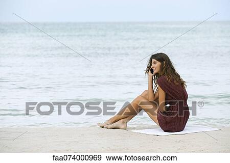 Young woman sitting on beach, using cell phone View Large Photo Image Stock Photo - Young woman sitting on beach, using cell phone. Fotosearch