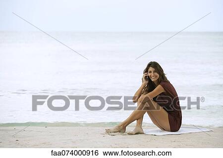 Young woman sitting on beach, using cell phone View Large Photo Image Stock Photograph - Young woman sitting on beach, using cell phone. Fotosearch