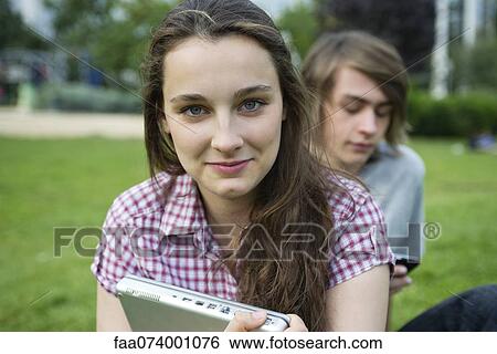 Stock Photograph - Young woman sitting outdoors, holding laptop computer, portrait. Fotosearch