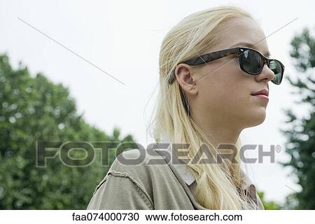 Stock Image - Young woman wearing sunglasses, looking away in thought. Fotosearch