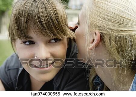Stock Photography - Young woman whispering in her friend's ear. Fotosearch