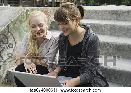 Stock Image - Young women looking at laptop computer together outdoors. Fotosearch