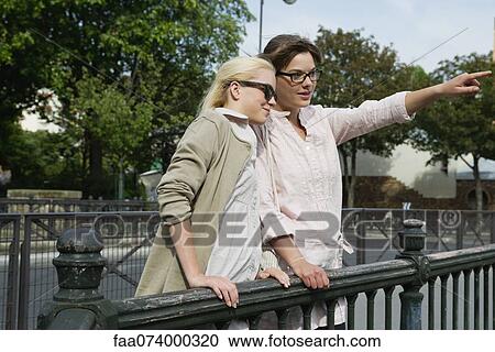 Young women standing together outdoors, looking at something out of frame View Large Photo Image Stock Image - Young women standing together outdoors, looking at something out of frame. Fotosearch