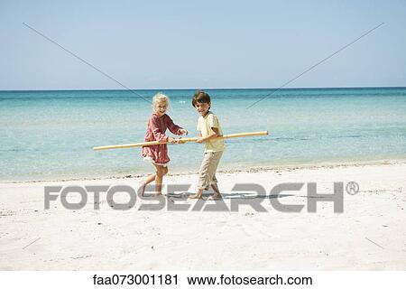 Stock Image - Boy and girl holding stick together on beach. Fotosearch