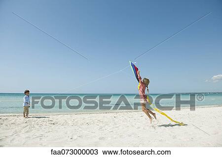Stock Image - Boy flying kite on beach, girl jumping to catch. Fotosearch