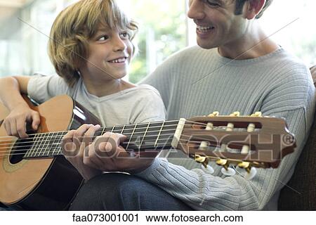Boy learning how to play guitar with father View Large Photo Image Stock Image - Boy learning how to play guitar with father. Fotosearch