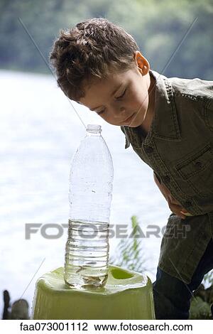 Stock Image - Boy looking at fish in water bottle. Fotosearch