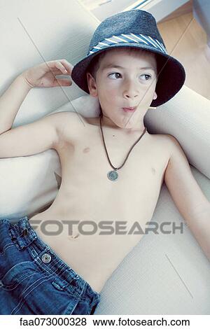 Stock Photo - Boy lying on sofa, eating lollilop, portrait. Fotosearch