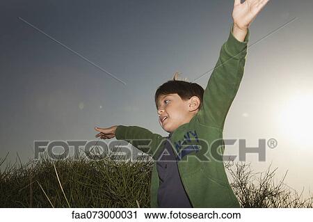 Boy playing outdoors with arms raised in air View Large Photo Image Stock Image - Boy playing outdoors with arms raised in air. Fotosearch