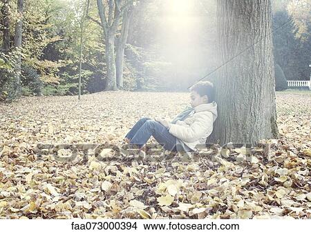 Boy sitting under tree in autumn leaves, portrait View Large Photo Image Picture - Boy sitting under tree in autumn leaves, portrait. Fotosearch