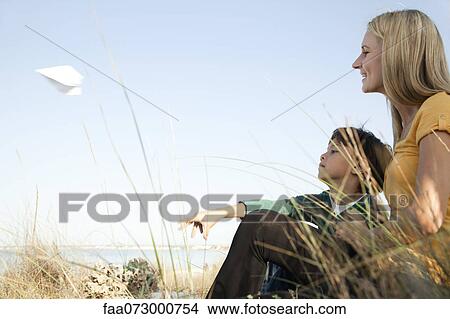 Boy sitting with his mother, throwing paper airplane View Large Photo Image Picture - Boy sitting with his mother, throwing paper airplane. Fotosearch