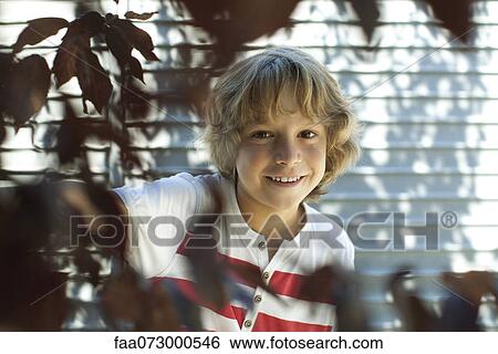 Stock Photograph - Boy smiling behind tree branches. Fotosearch