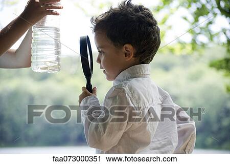 Boy studying fish in water bottle with magnifying glass View Large Photo Image Stock Image - Boy studying fish in water bottle with magnifying glass. Fotosearch