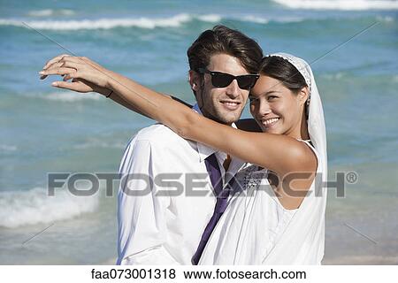 Stock Photo - Bride and groom embracing at the beach, portrait. Fotosearch