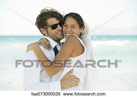 Stock Photography - Bridge and groom embracing at the beach, portrait. Fotosearch