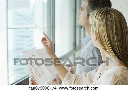 Business associates holding blueprints and looking out window View Large Photo Image Picture - Business associates holding blueprints and looking out window. Fotosearch