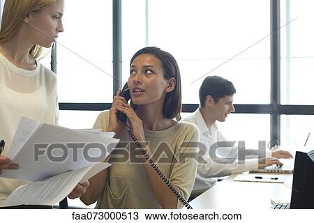 Businesswoman talking on phone in office, looking at colleague View Large Photo Image Stock Image - Businesswoman talking on phone in office, looking at colleague. Fotosearch