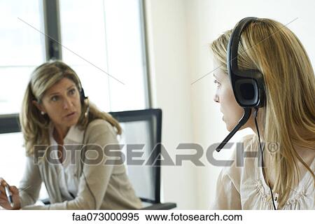 Stock Photography - Businesswomen talking together in office, both wearing headsets. Fotosearch