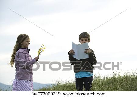 Children in field, boy reading book while girl picks wildflowers View Large Photo Image Stock Photo - Children in field, boy reading book while girl picks wildflowers. Fotosearch