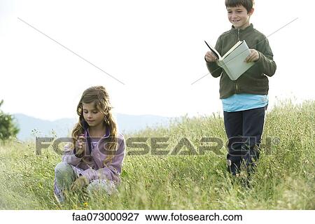 Children in field, boy reading book while girl picks wildflowers View Large Photo Image Stock Photo - Children in field, boy reading book while girl picks wildflowers. Fotosearch