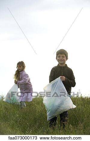 Stock Image - Children picking up trash in field. Fotosearch