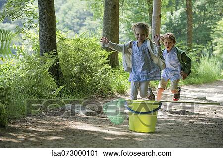 Stock Image - Children running toward bucket and butterfly net in woods. Fotosearch