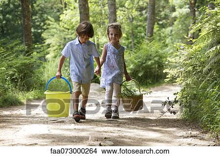 Children walking hand in hand in woods, carrying basket and bucket View Large Photo Image Picture - Children walking hand in hand in woods, carrying basket and bucket. Fotosearch